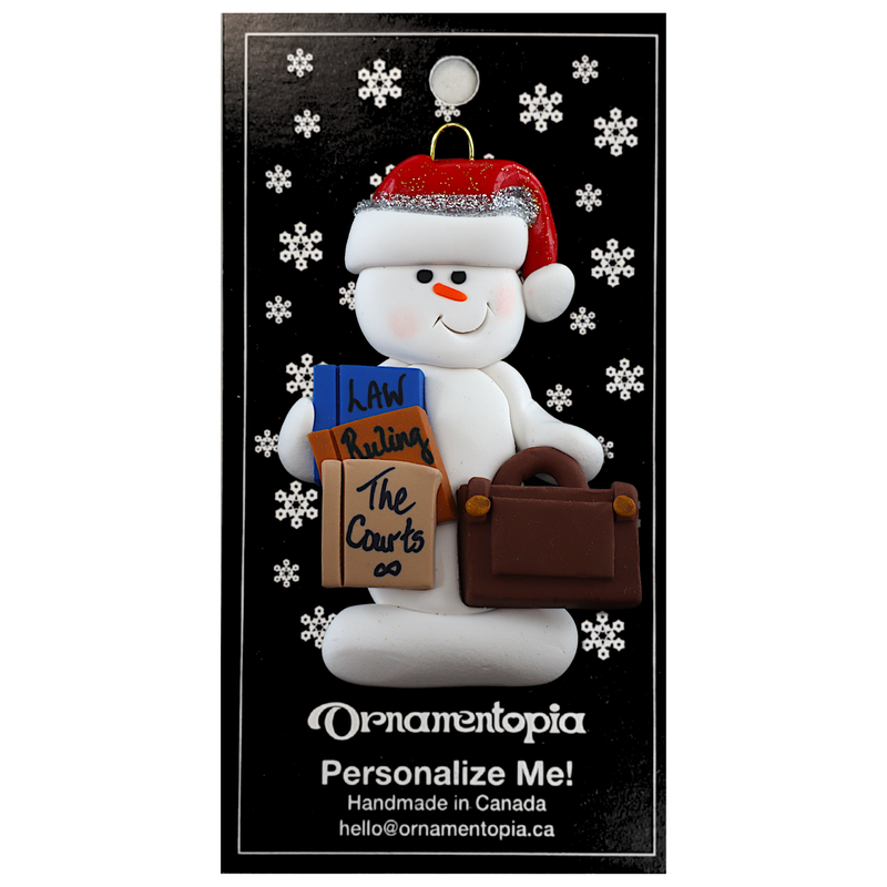 Ornament of white snowman in red hat holding a briefcase and law books, on display backing card.
