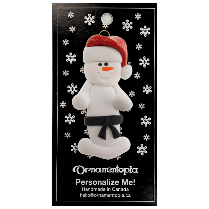 Ornament of white snowman in red hat wearing black belt, on display backing card.