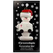 Ornament of white snowman in red hat holding a white ambulance, on display backing card.