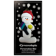 Ornament of white snowman in red hat holding a pickleball paddle and yellow pickleball, on display backing card.