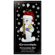 Ornament of white snowman in red hat holding a pool cue and pool balls, on display backing card.