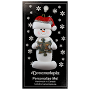 Ornament of white snowman in red hat holding a puzzle piece, on display backing card.