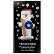 Ornament of white snowman in red hat holding a ringette stick and blue ring, on display backing card.