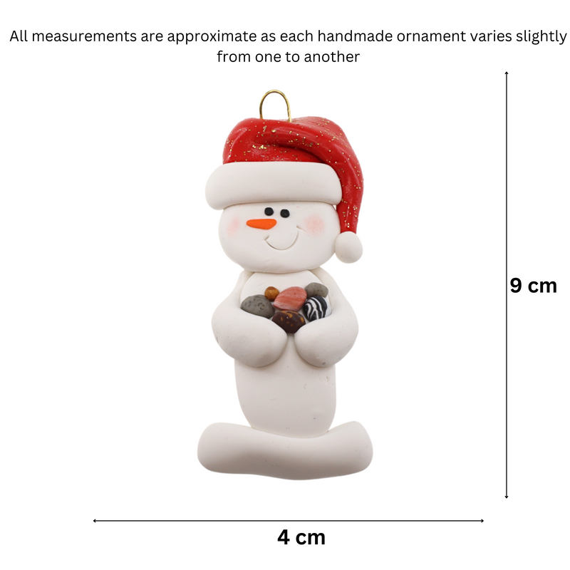 Ornament of white snowman in red hat holding several small rocks, graphed to show size (4x9cm).