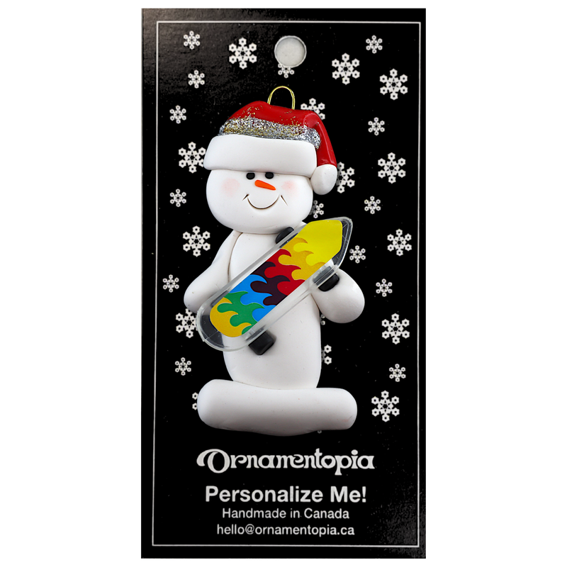Ornament of white snowman in red hat holding a vibrant skateboard, on display backing card.