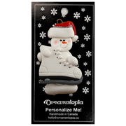 Ornament of white snowman in red hat holding a large white ice skate, on display backing card.