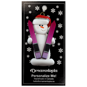 Ornament of white snowman in red hat holding a pair of vibrant skis, on display backing card.