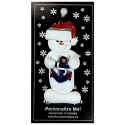 Ornament of white snowman in red hat holding a plastic anchor, on display backing card.