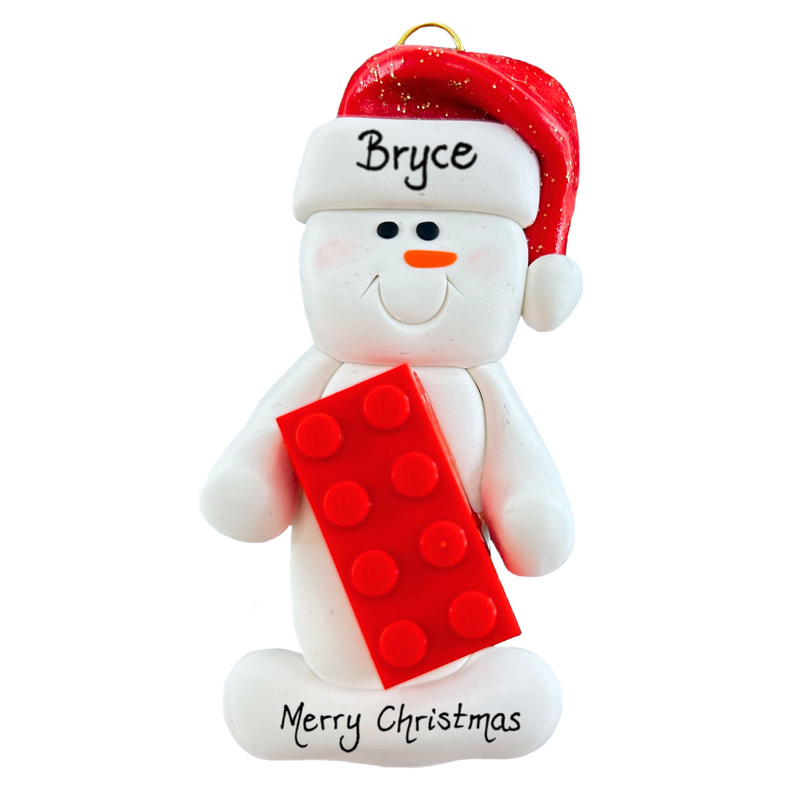Ornament of white snowman in red hat holding a plastic building brick, personalized with name.