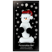 Ornament of white snowman in red hat holding black cheerleader pom-poms, on display backing card.
