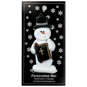 Ornament of white snowman in black top hat, holding a Bible, on display backing card.