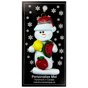 Ornament of white snowman in red hat holding various fruits, on display backing card.
