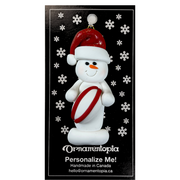 Ornament of white snowman in red hat holding a red and white rugby ball, on display backing card.