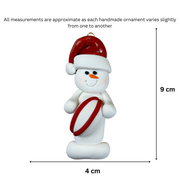 Ornament of white snowman in red hat holding a red and white rugby ball, graphed to show size (4x9cm).