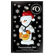 Ornament of white snowman in red hat holding chicken and stethoscope, on display backing card.