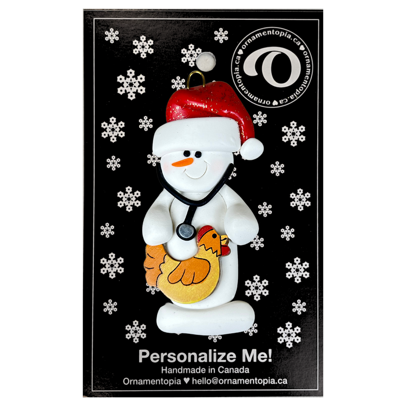 Ornament of white snowman in red hat holding chicken and stethoscope, on display backing card.