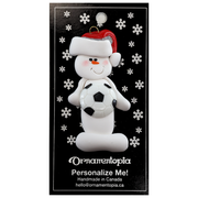 Ornament of white snowman in red hat holding a soccer ball, on display backing card.