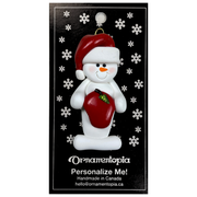 Ornament of white snowman in red hat holding a shiny red apple, on display backing card.