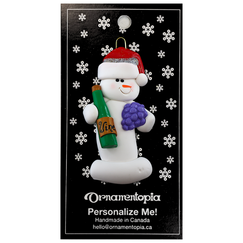Ornament of white snowman in red hat holding a cluster of grapes and a wine bottle, on display backing card.