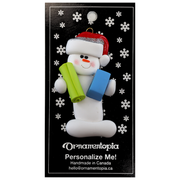 Ornament of white snowman in red hat holding vibrant yoga mat and block, on display backing card.