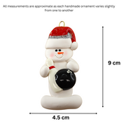 Ornament of white snowman in red hat holding a black bowling ball and pin, graphed to show size (4.5x9cm).
