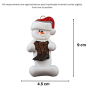 Ornament of white snowman in red hat holding cowboy boots, graphed to show size (4.5x9cm).
