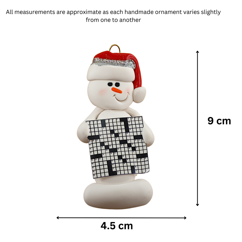 Ornament of white snowman in red hat holding large crossword puzzle, graphed to show size (4.5x9cm).