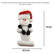Ornament of white snowman in red hat carrying two dumbbells, graphed to show size (4.5x9cm).