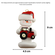 Ornament of white snowman in red hat holding a red tractor, graphed to show size (4.5x9cm).