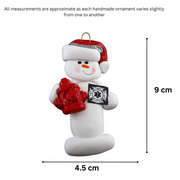 Ornament of white snowman in red hat holding a fire hydrant and firefighter badge, graphed to show size (4.5x9cm).