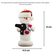 Ornament of white snowman in red hat holding a hairdryer and bottle of hair product, graphed to show size (4.5x9cm).