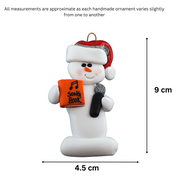 Ornament of white snowman in red hat holding a microphone and orange music book, graphed to show size (4.5x9cm).