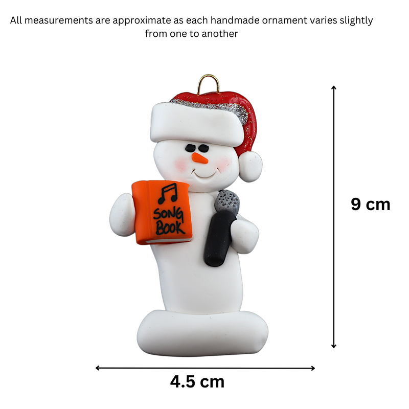 Ornament of white snowman in red hat holding a microphone and orange music book, graphed to show size (4.5x9cm).