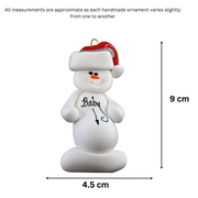 Ornament of white snowman in red hat with a round stomach that says “baby”, graphed to show size (4.5x9cm).