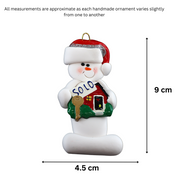 Ornament of white snowman in red hat holding a sign with a house saying “sold”, graphed to show size (4.5x9cm).