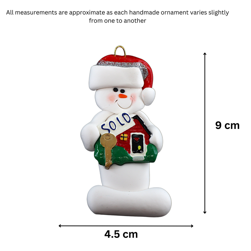 Ornament of white snowman in red hat holding a sign with a house saying “sold”, graphed to show size (4.5x9cm).