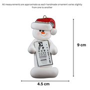 Ornament of white snowman in red hat holding an eye chart, graphed to show size (4.5x9cm).