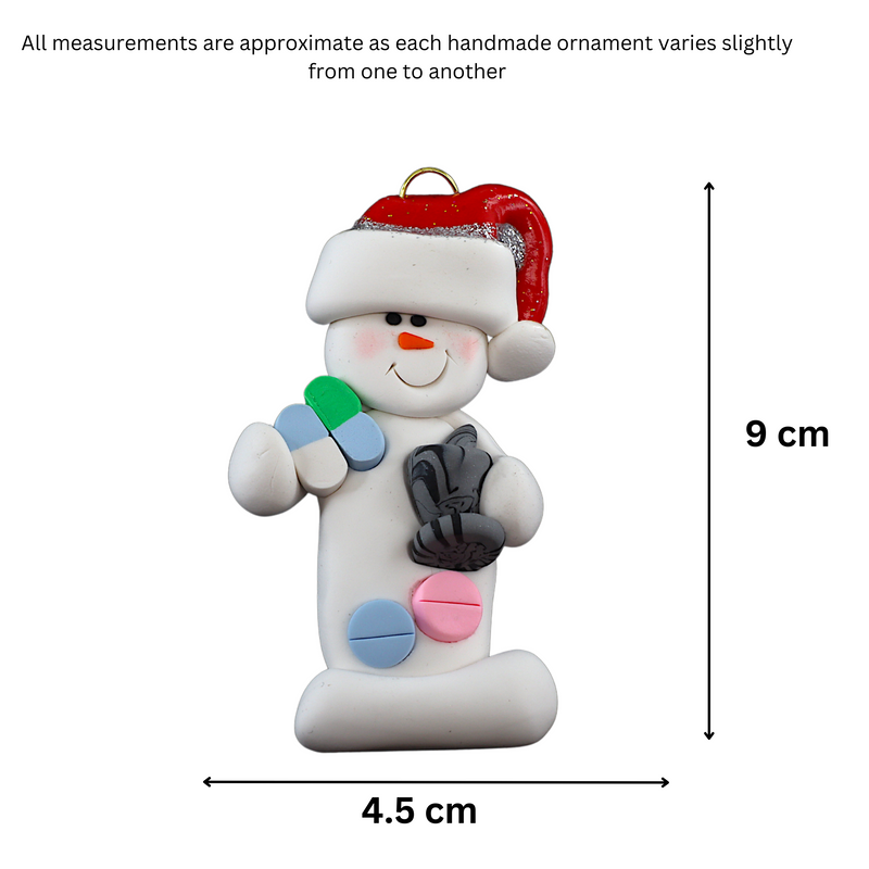 Ornament of white snowman in red hat holding various pills and a mortar and pestle, graphed to show size (4.5x9cm).