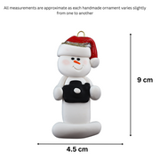 Ornament of white snowman in red hat holding a black camera, graphed to show size (4.5xcm).