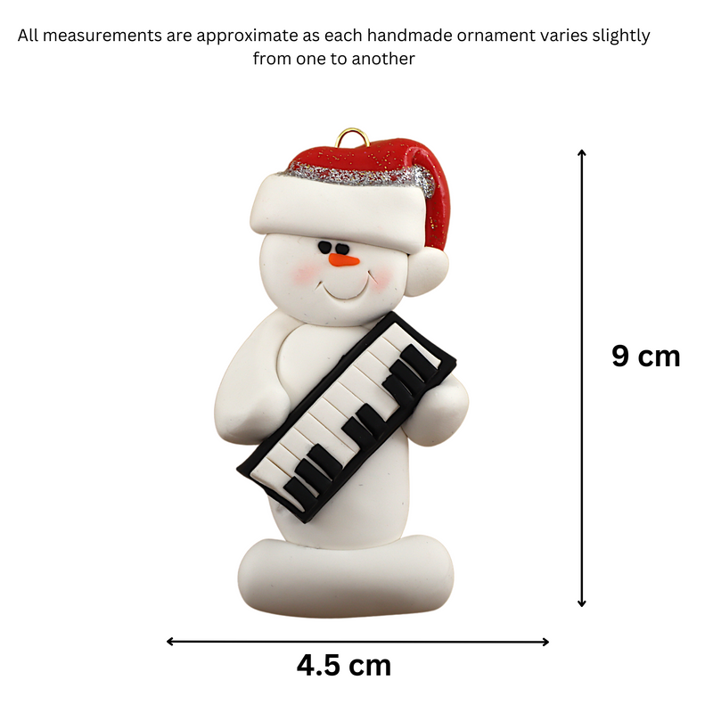 Ornament of white snowman in red hat holding a piano keyboard, graphed to show size (4.5x9cm).