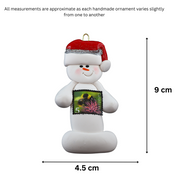 Ornament of white snowman in red hat holding a postal stamp, graphed to show size (4.5x9cm).
