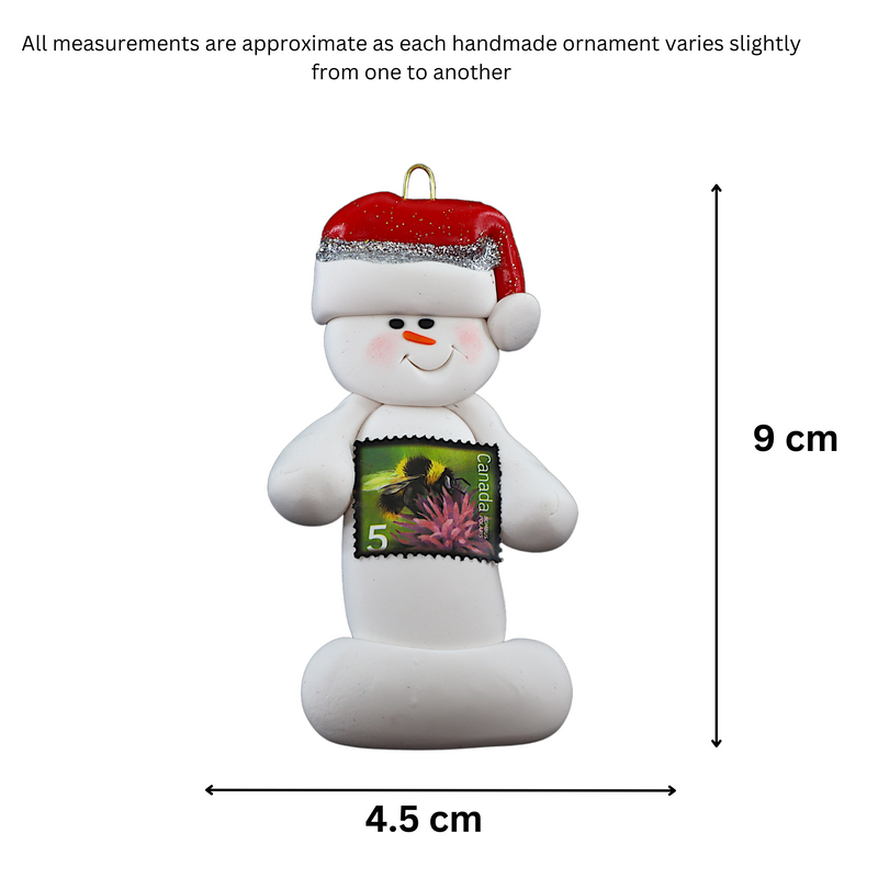 Ornament of white snowman in red hat holding a postal stamp, graphed to show size (4.5x9cm).
