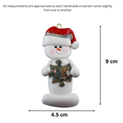 Ornament of white snowman in red hat holding a puzzle piece, graphed to show size (4.5x9cm).