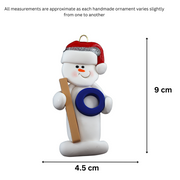 Ornament of white snowman in red hat holding a ringette stick and blue ring, graphed to show size (4.5x9cm).