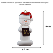 Ornament of white snowman in red hat holding a scrabble tile, graphed to show size (4.5x9cm).