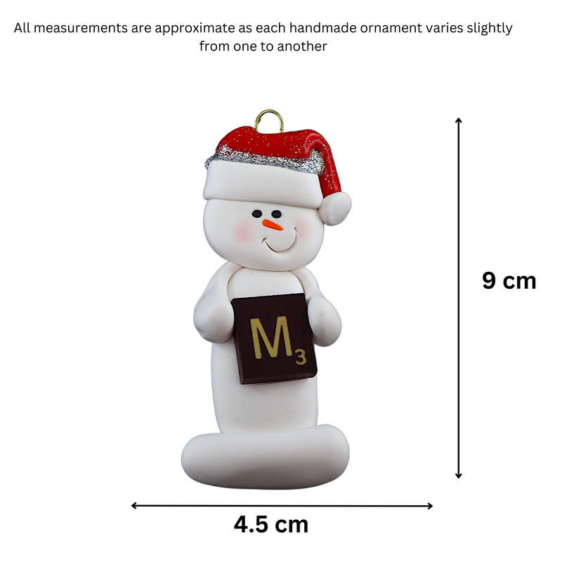 Ornament of white snowman in red hat holding a scrabble tile, graphed to show size (4.5x9cm).