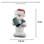 Ornament of white snowman in red hat holding a spool of thread and scissors, graphed to show size (4.5x9cm).