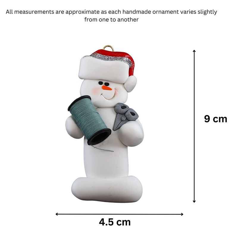 Ornament of white snowman in red hat holding a spool of thread and scissors, graphed to show size (4.5x9cm).