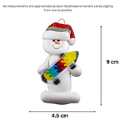 Ornament of white snowman in red hat holding a vibrant skateboard, graphed to show size (4.5x9cm).