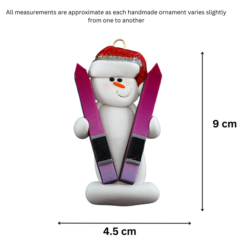 Ornament of white snowman in red hat holding a pair of vibrant skis, graphed to show size (4.5x9cm).